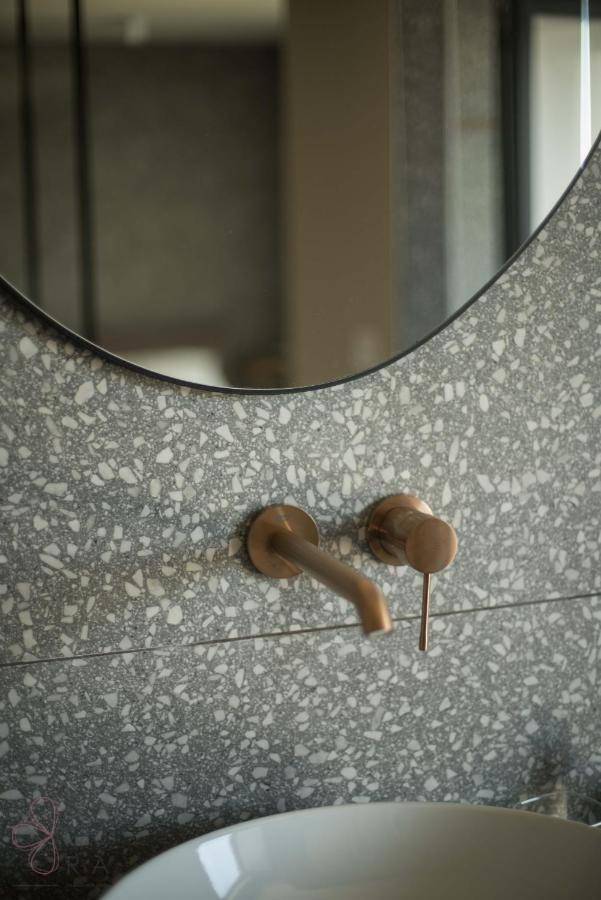 Modernes Badezimmer mit Terrazzo-Fliesen, Wandarmatur und elegantem runden Spiegel.