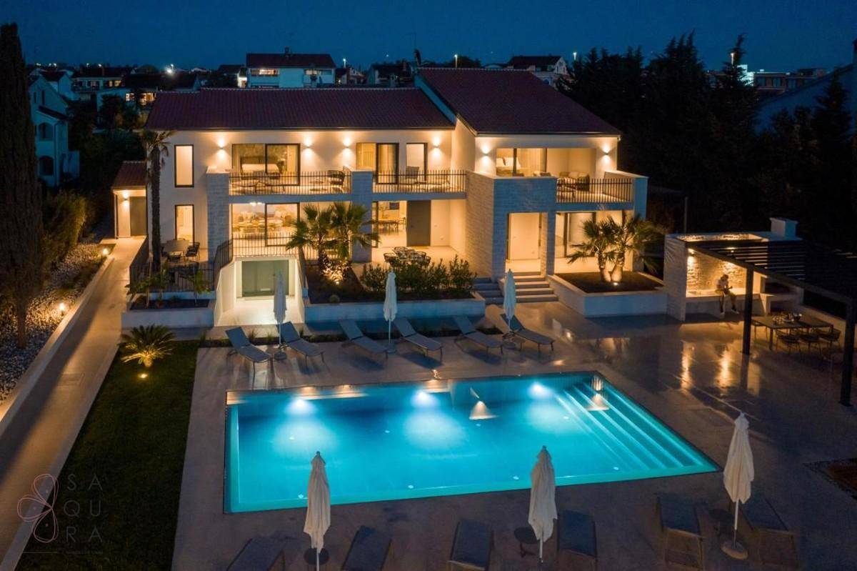 Luxuriöse Villa mit beleuchtetem Pool und Terrassen bei Nacht, einladend und elegant.