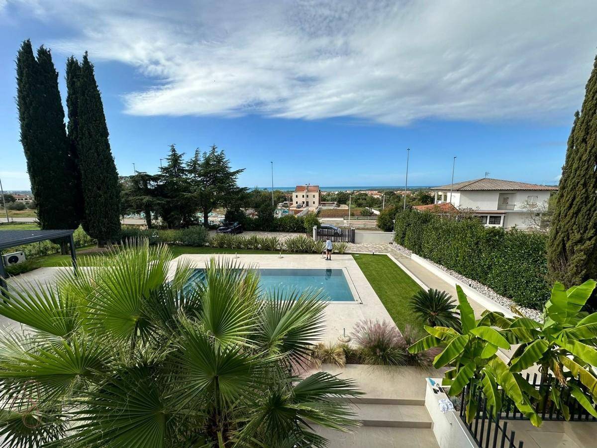 Gepflegter Gartenbereich mit Pool, Palmen und einem weiten Blick auf das Meer am Horizont.