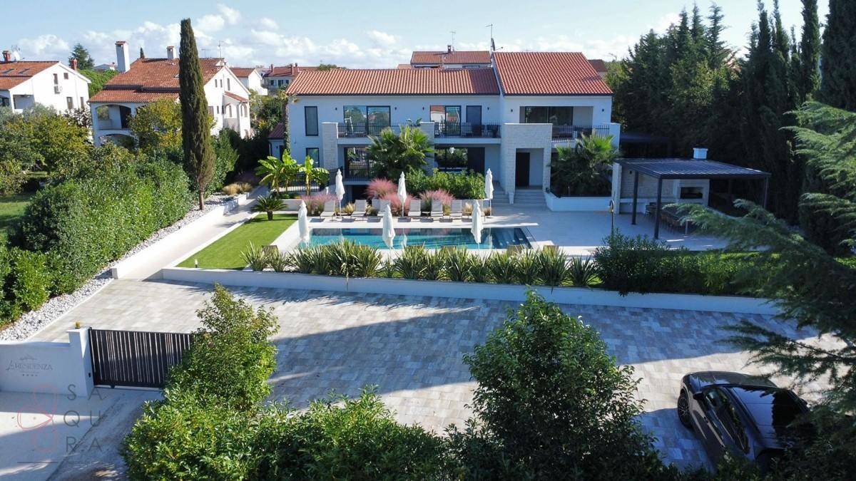 Luxuriöse Villa mit großem Pool, gepflegtem Garten und privater Zufahrt, umgeben von Grün.