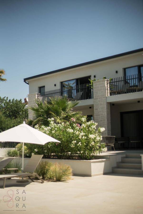 Elegante Villa mit Poolbereich, Liegestühlen und üppiger mediterraner Vegetation im Sonnenschein.