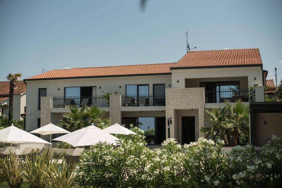 Moderne Villa mit Terrassen, Balkonen und mediterraner Bepflanzung unter blauem Himmel.