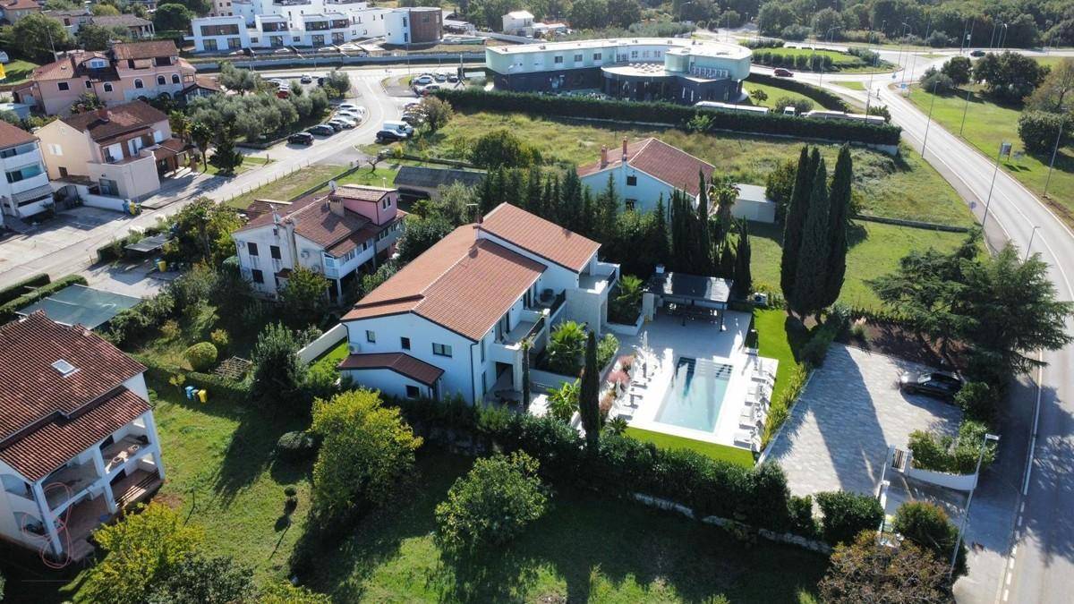 Panoramablick auf die moderne Villa mit Poolbereich, umgeben von Wohngebäuden und einer Straße.