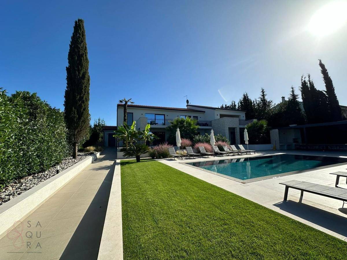 Weitläufiger Garten mit Pool, Liegewiese und moderner Villa unter strahlendem Himmel.