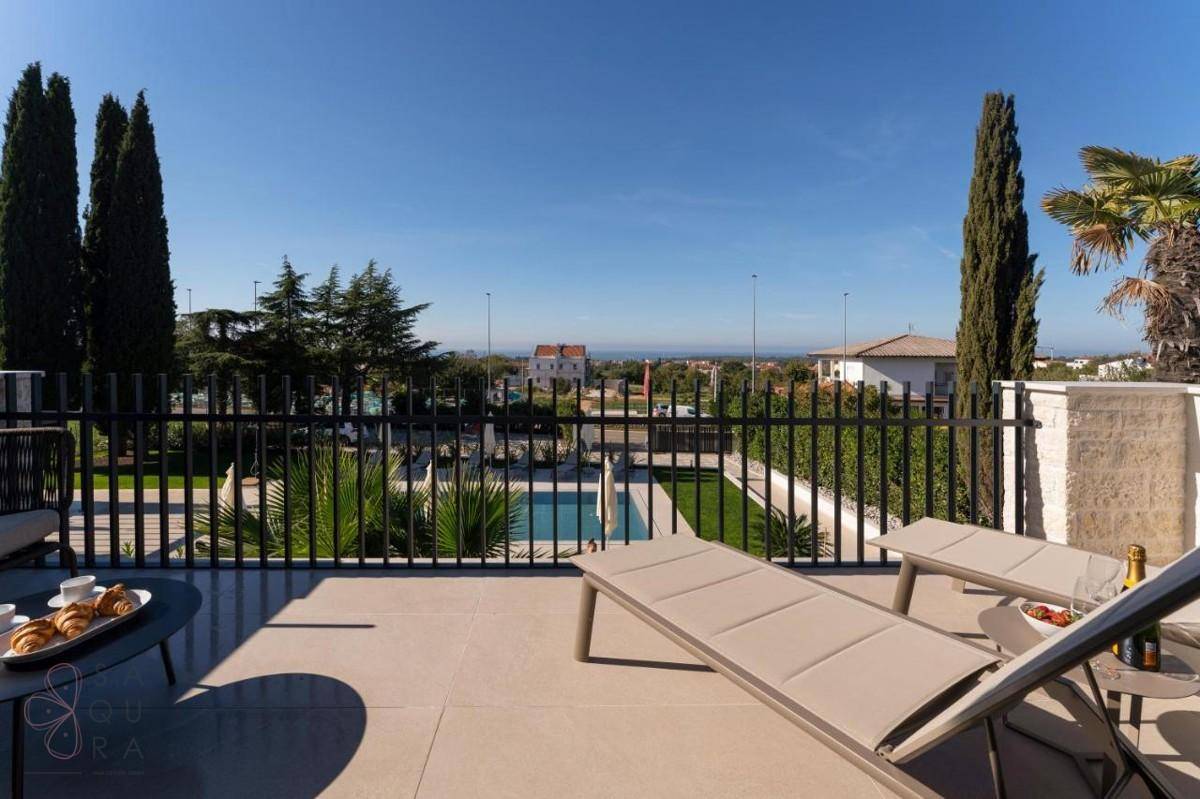 Geräumige Terrasse mit Liegestühlen, Blick auf den Pool und die grüne Umgebung unter blauem Himmel.