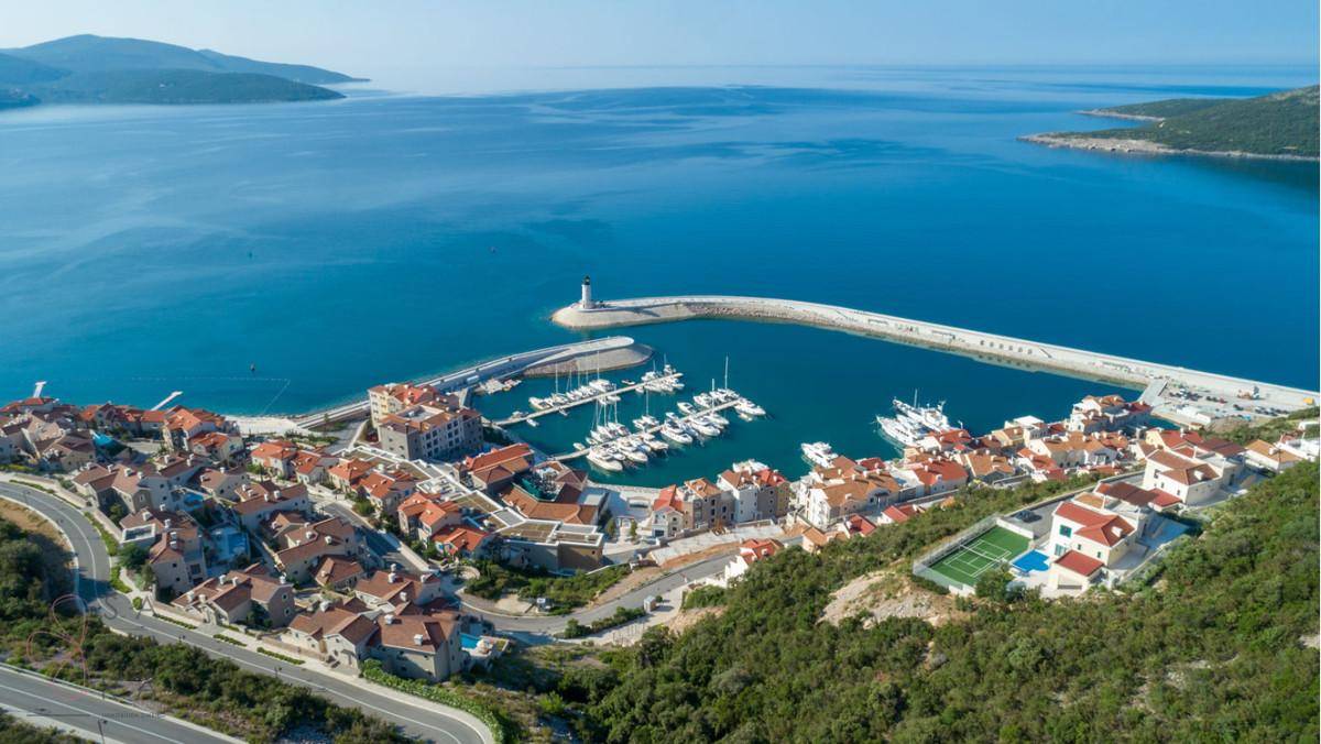 Panoramablick auf eine malerische Küstenstadt mit Yachthafen, Leuchtturm und vielen Häusern am Meer.