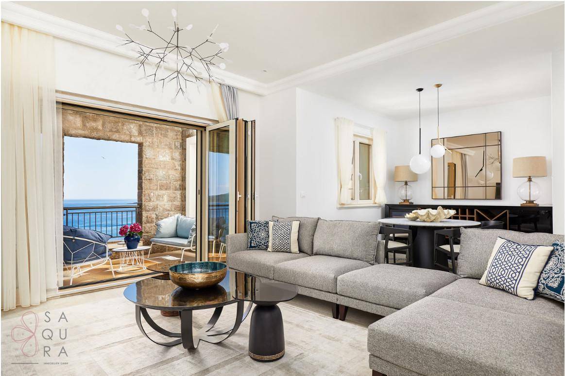 Moderner Wohn- und Essbereich mit großem Sofa und Zugang zu einem Balkon mit Meerblick.