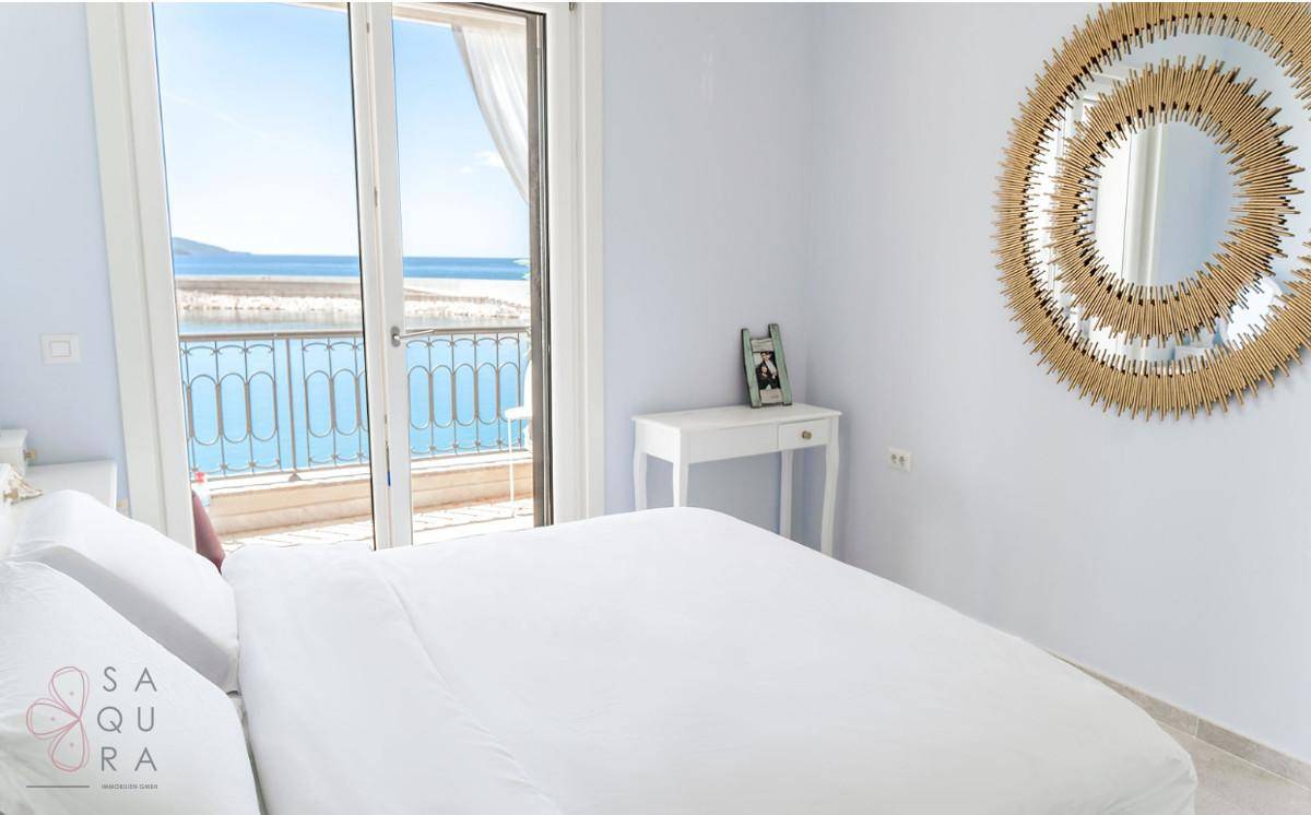 Helles Schlafzimmer mit Meerblick, Balkonzugang und einem dekorativen Spiegel.
