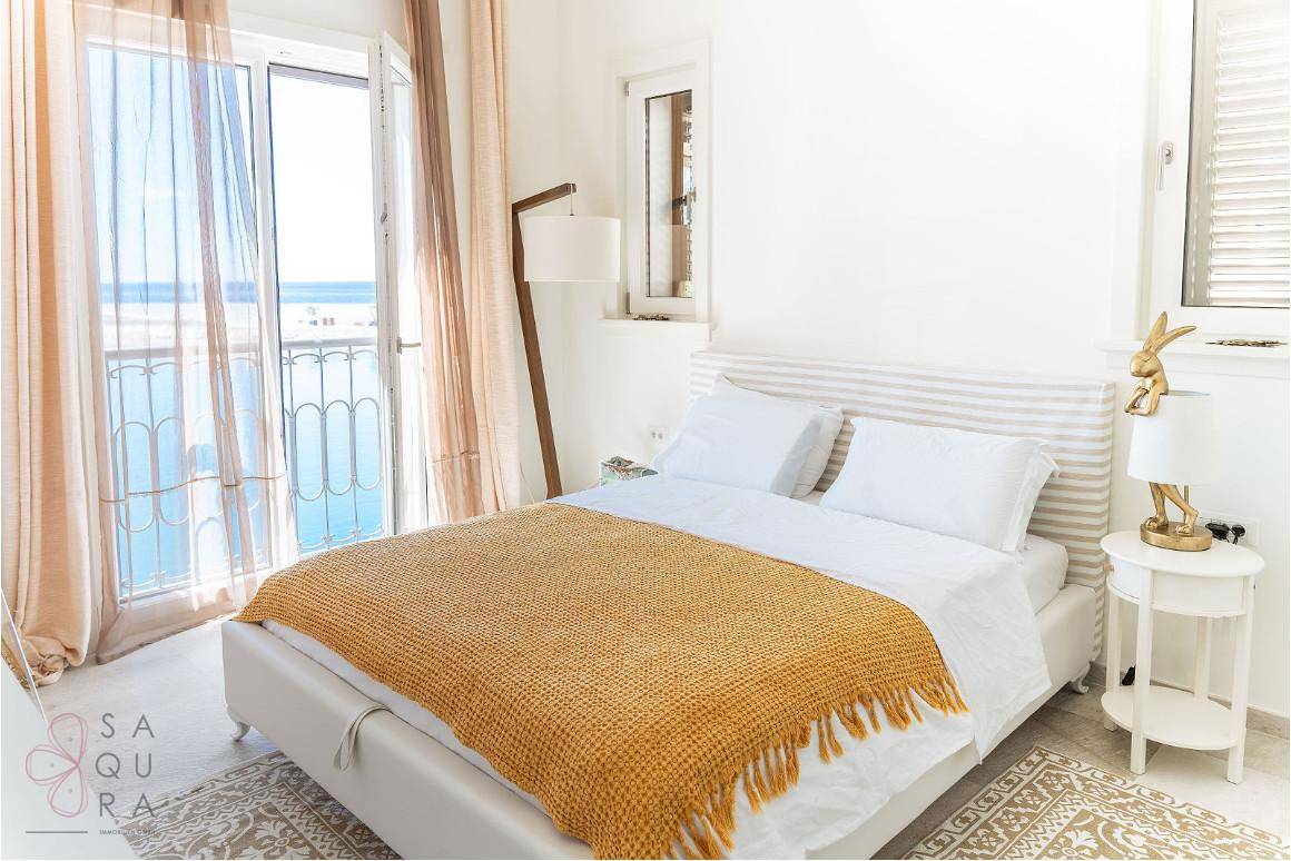 Helles Schlafzimmer mit Meerblick, Balkonzugang und einem warmen Farbakzent.