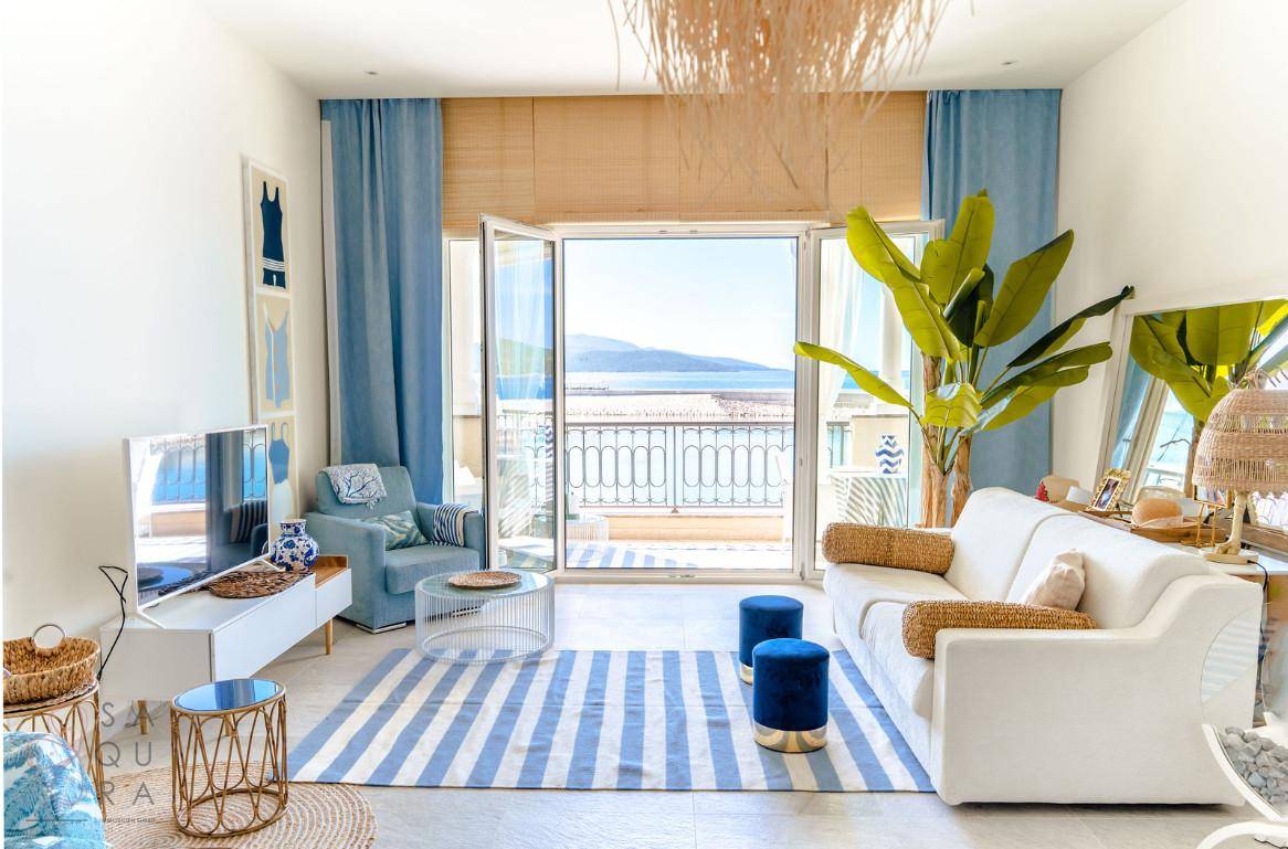 Farbenfrohes Wohnzimmer mit weißem Sofa, blauen Akzenten und Balkonzugang mit Meerblick.