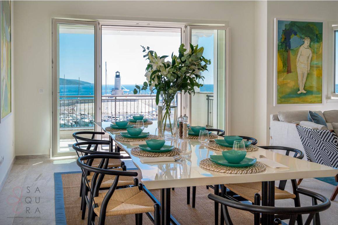 Heller Essbereich mit großem Tisch und Blick auf den Yachthafen und Leuchtturm durch Panoramafenster.