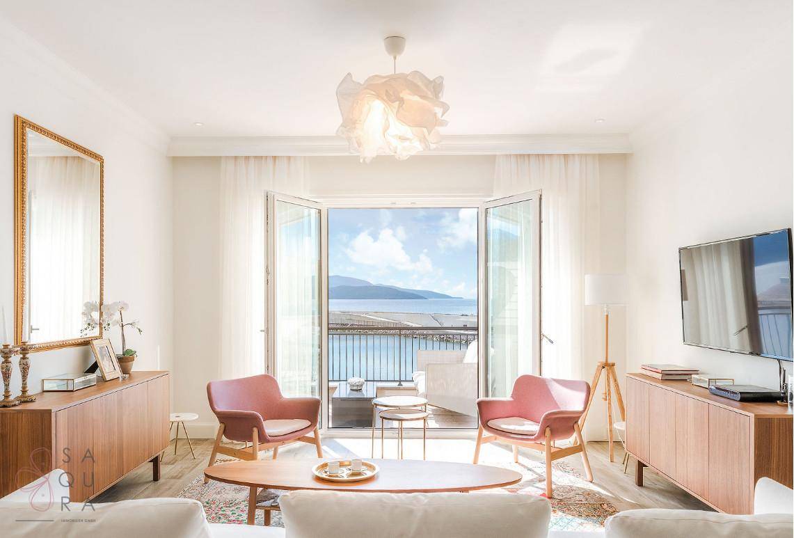 Elegantes Wohnzimmer mit zwei rosa Sesseln, Holzmöbeln und Balkonzugang mit Meerblick.