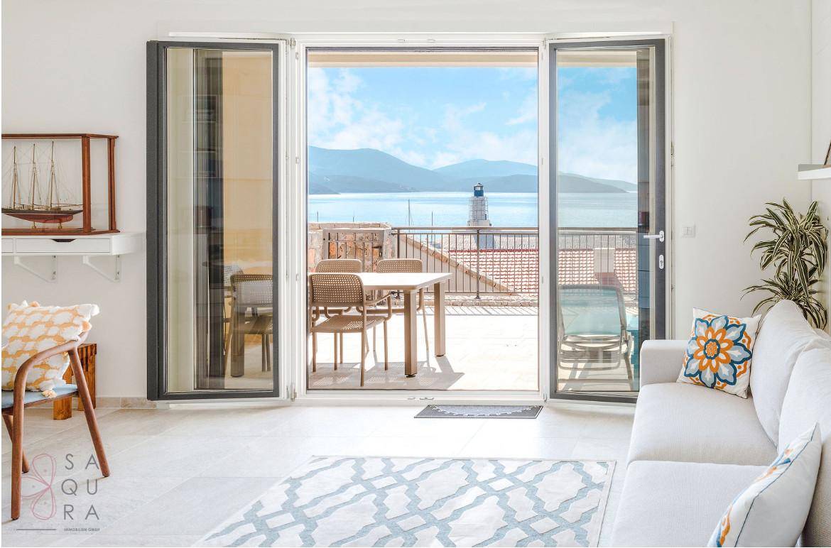 Helles Wohnzimmer mit weißem Sofa und großen Falttüren zu einem Balkon mit Meer- und Leuchtturmblick.