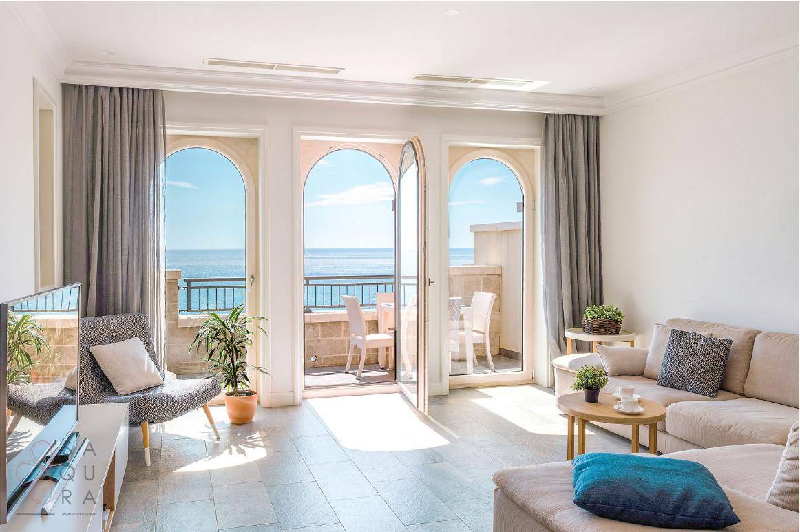 Helles Wohnzimmer mit großen Bogenfenstern und direktem Zugang zu einem Balkon mit Meerblick.