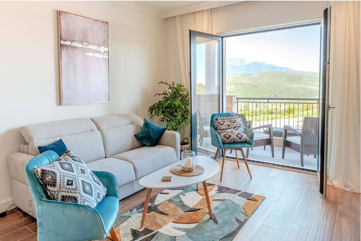 Helles Wohnzimmer mit beigem Sofa, blauen Akzenten und Zugang zu einem Balkon mit Bergblick.