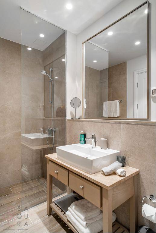 Modernes Badezimmer mit begehbarer Dusche, elegantem Waschtisch und großem Spiegel in neutralen Farbtönen.