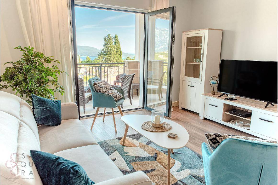 Helles Wohnzimmer mit bequemer Couch, Pflanzen und Zugang zu einem Balkon mit Meerblick.