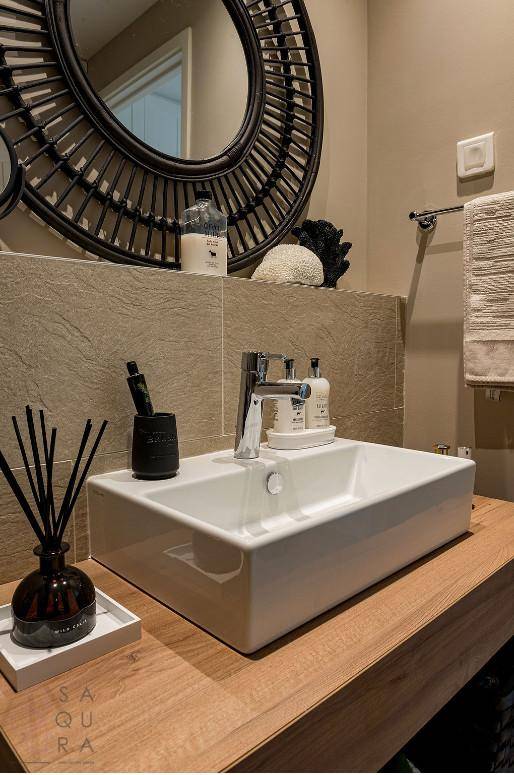 Modernes Badezimmer mit Aufsatzwaschbecken, Holzplatte und großem runden Spiegel.