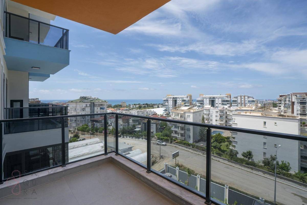 Geräumiger Balkon mit Glasgeländer und weitem Blick auf die Stadt und das Meer unter blauem Himmel.
