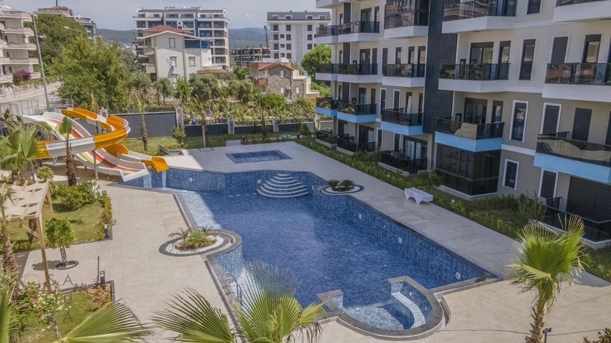 Großer Swimmingpool mit Wasserrutsche, Palmen und Liegebereich in einem modernen Wohnkomplex.