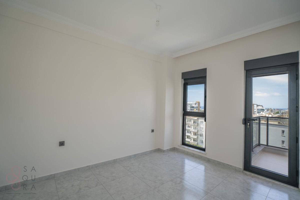 Leeres Schlafzimmer mit Fliesenboden, Fenster und Zugang zu einem kleinen Balkon.
