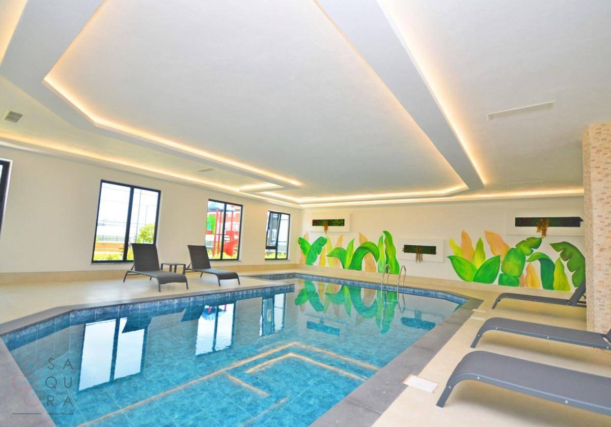 Heller Innenpool mit Liegestühlen und großen Fenstern, ideal zum Schwimmen und Entspannen.