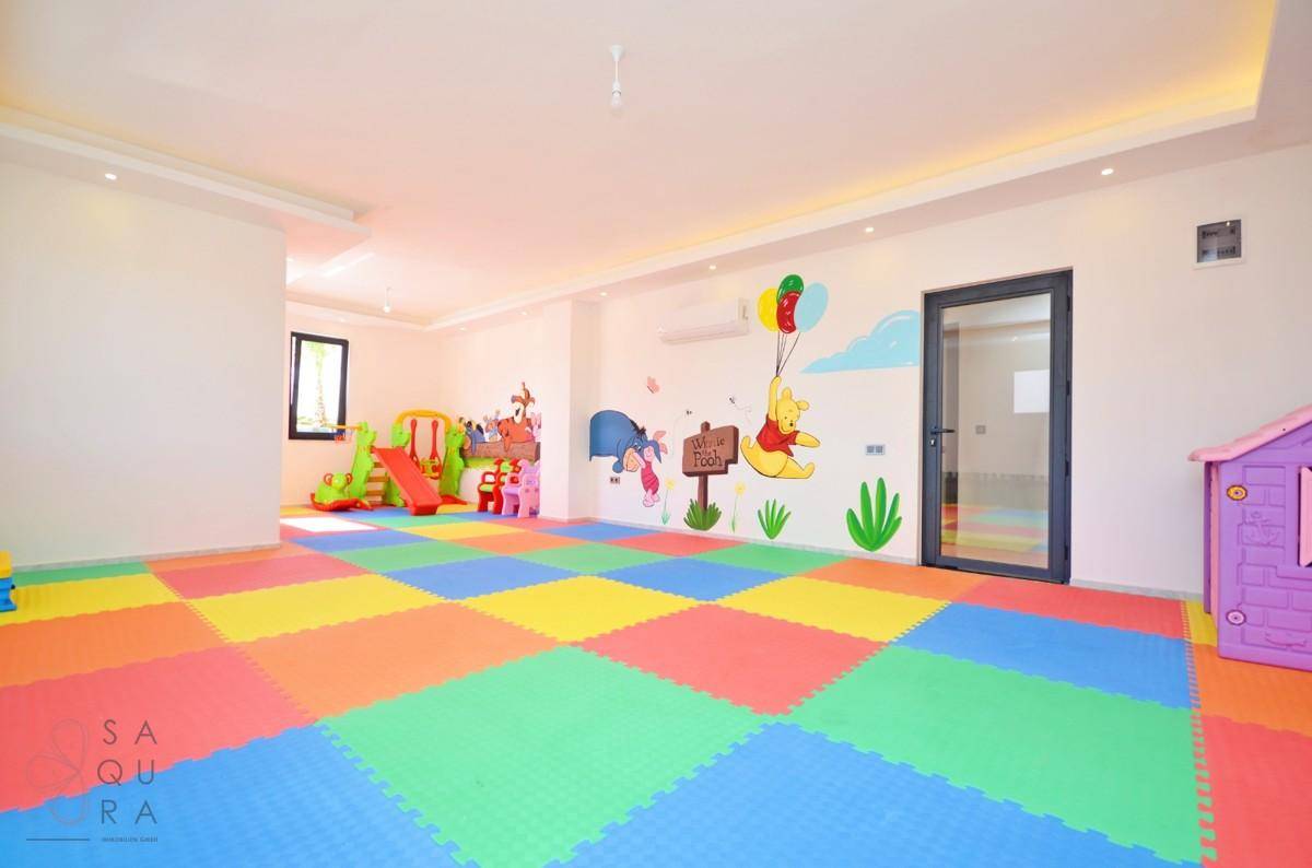 Heller und farbenfroher Spielraum mit bunten Bodenmatten, Wanddekorationen und Kinderspielgeräten.