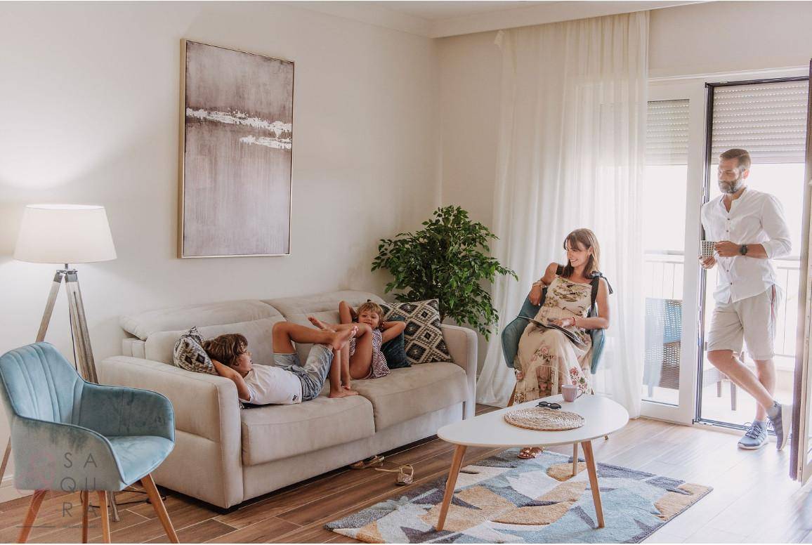 Helles Wohnzimmer mit Familie, bequemer Couch und Zugang zu einem sonnigen Balkon.