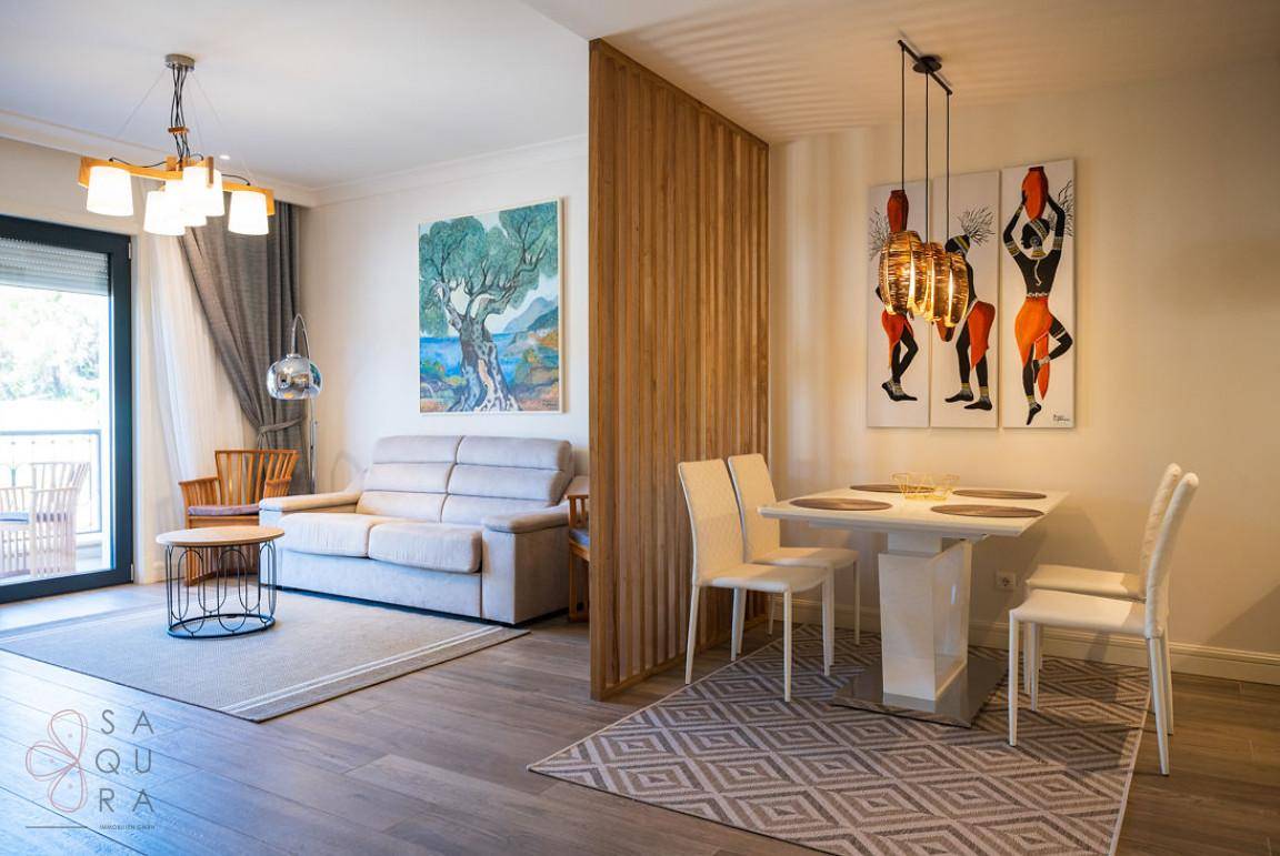 Heller Wohn-Essbereich mit stilvollem Holztrenner, modernen Möbeln und Zugang zum Balkon.