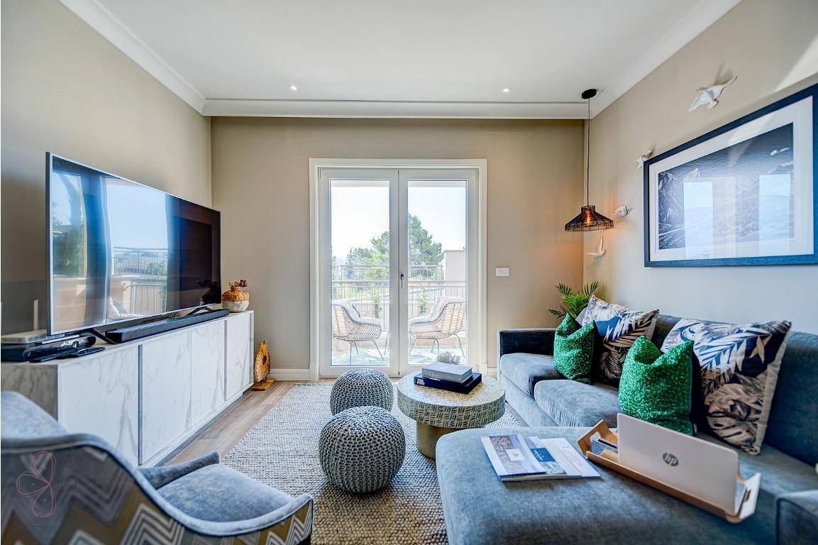Modernes Wohnzimmer mit großem Fernseher, beigem Sofa und Zugang zu einem sonnigen Balkon.