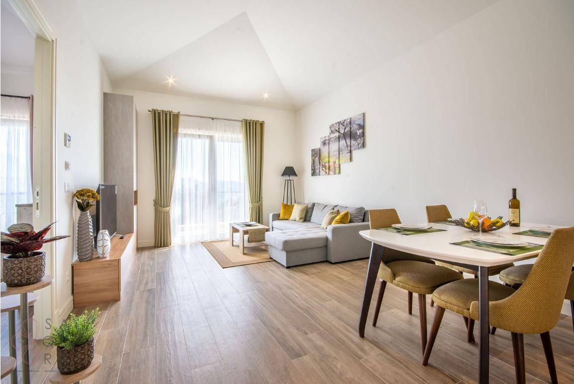 Geräumiger Wohn-Essbereich mit hellem Holzboden, großem Esstisch und Zugang zum Balkon.