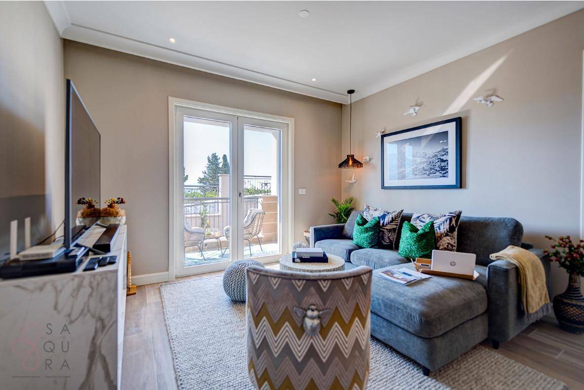 Modernes Wohnzimmer mit beigem Sofa, Fernseher und Zugang zu einem sonnigen Balkon.