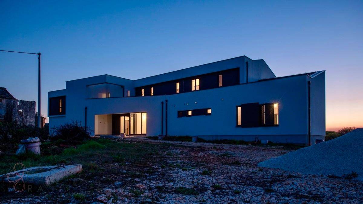 Moderne Villa in der Dämmerung, mit beleuchteten Fenstern und klarem Abendhimmel.