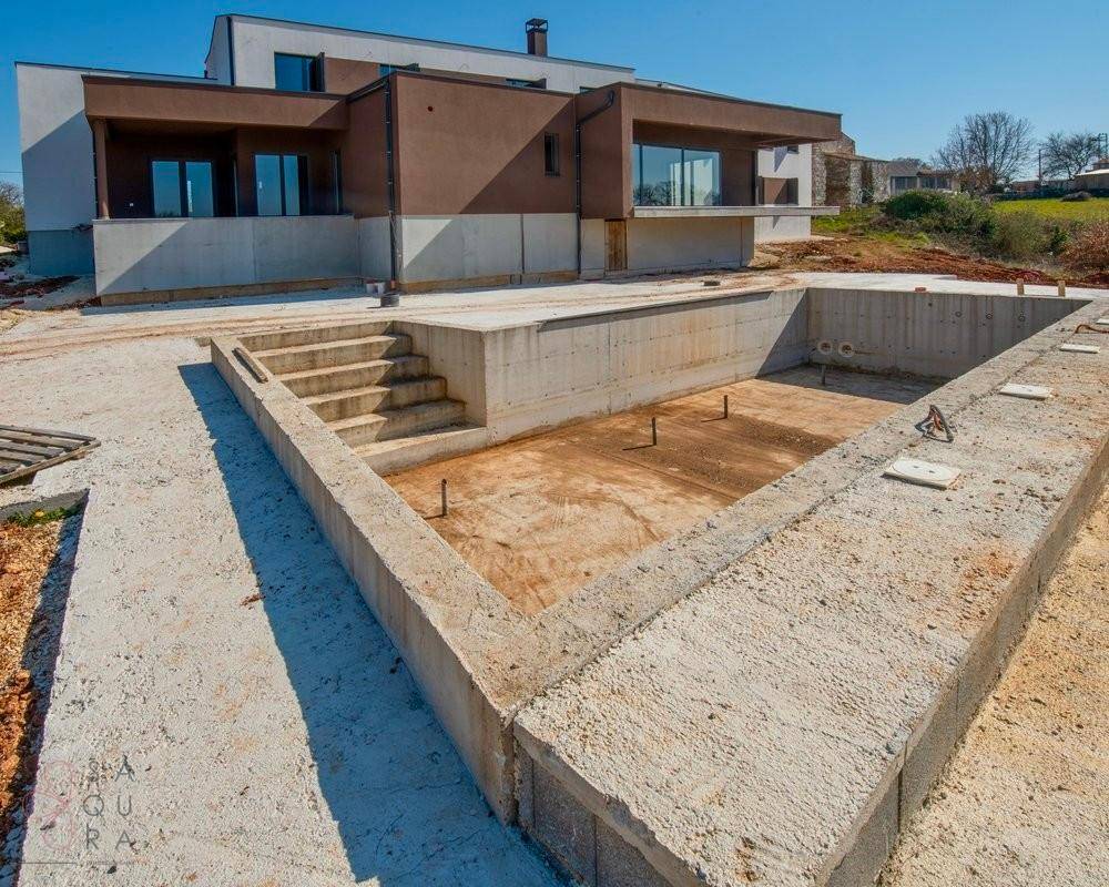 Unfertiger Poolbereich mit Betontreppen und Blick auf die moderne Villa im Hintergrund.