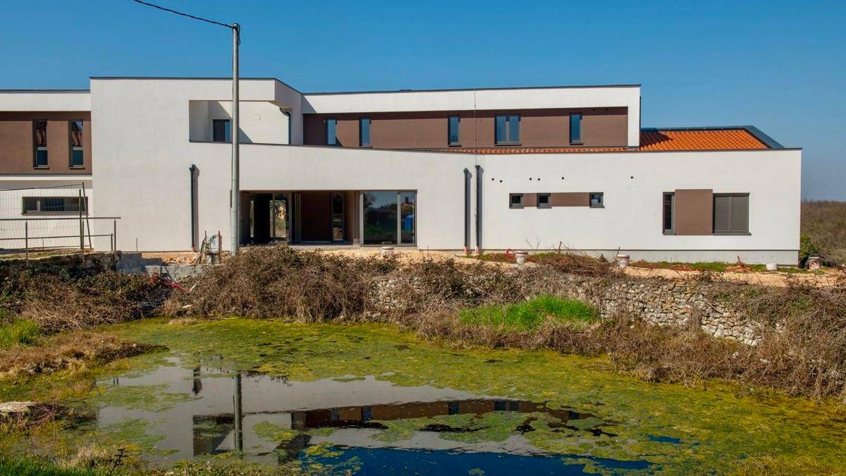 Moderne Villa mit weißer Fassade, die sich in einem natürlichen Teich spiegelt.