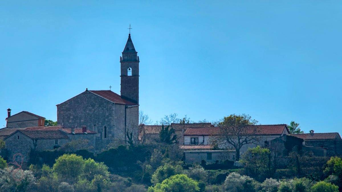 Malerische Ansicht eines historischen Dorfes mit Kirchturm unter strahlend blauem Himmel.