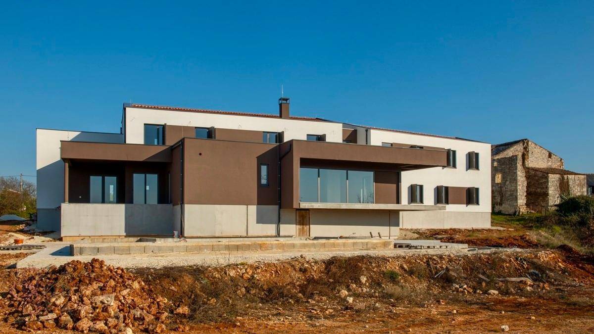 Moderne Villa im Bau mit Rohbau des Pools und Blick auf das angrenzende alte Gebäude.