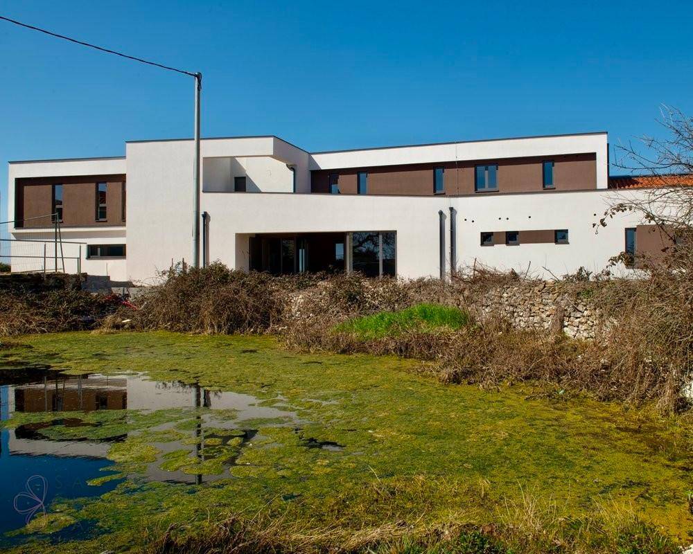 Moderne Villa mit weißer Fassade, reflektiert in einem natürlichen Teich im Vordergrund.