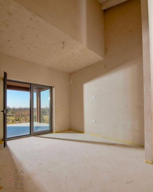 Unfertiger Wohnraum mit viel Tageslicht, großen Fensterfronten und Zugang zum Außenbereich.