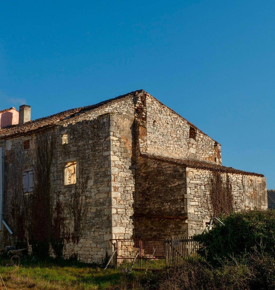 Altes Steinhaus mit bewachsenen Mauern, das den Kontrast zur modernen Neubauvilla bildet.
