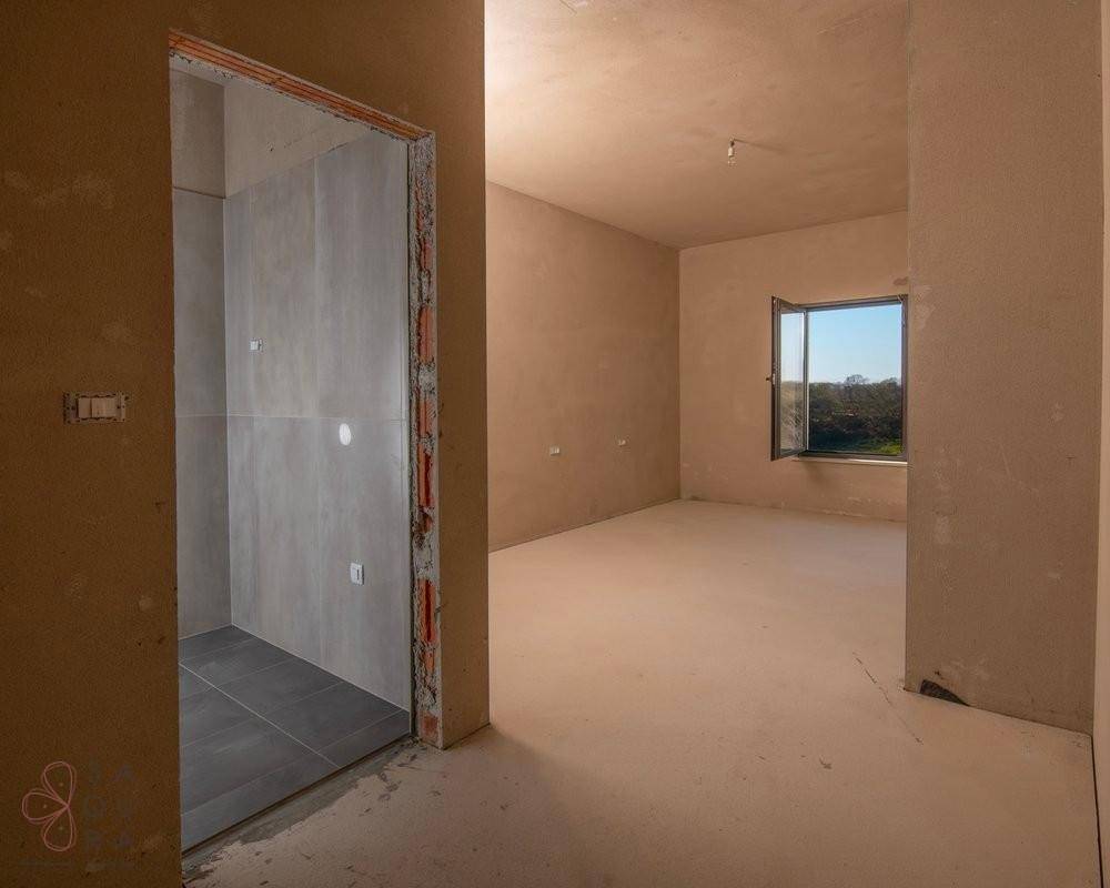 Unfertiges Zimmer mit Blick in ein gefliestes Badezimmer und Fenster, vielseitig nutzbar.