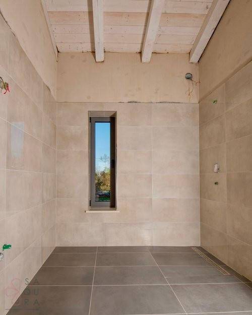 Unfertiges Badezimmer mit Fliesen an Wänden und Boden sowie einem schmalen Fenster.