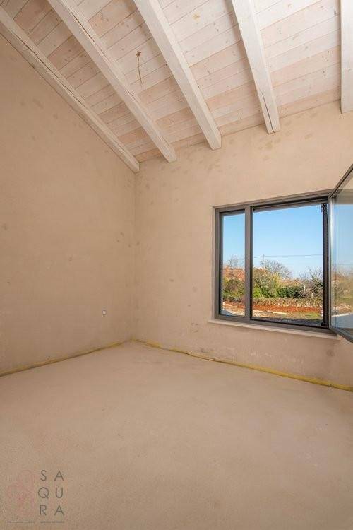 Unfertiges Zimmer mit sichtbaren Holzbalken an der Dachschräge und Fensterblick ins Grüne.