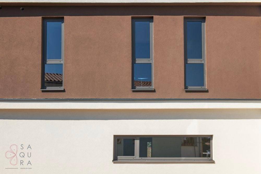 Fassadendetail mit vertikalen Fenstern in braunen und horizontalen Fenstern in weißen Wandbereichen.