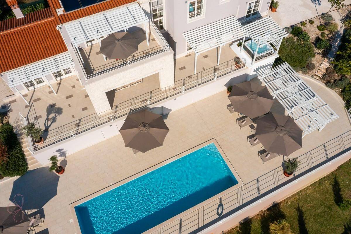 Detailansicht der Poolterrasse mit Liegestühlen, Sonnenschirmen und Whirlpool.