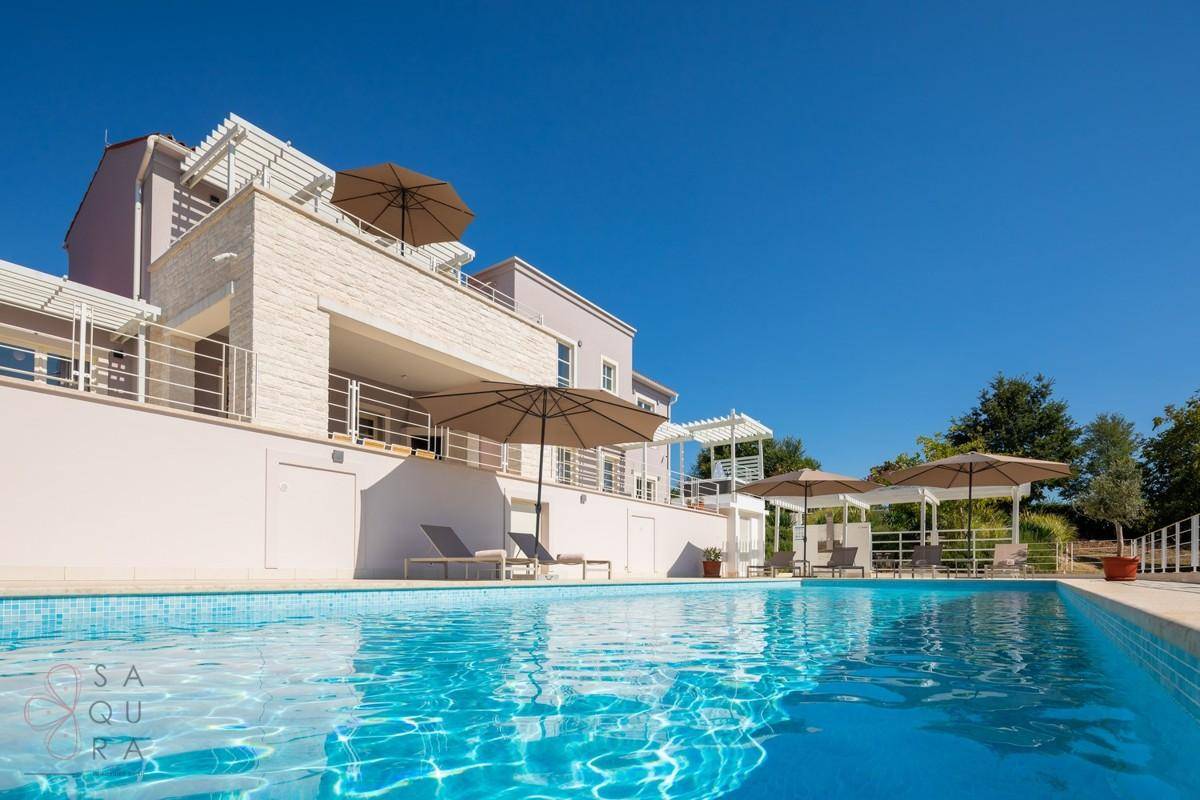 Blick vom Pool auf die elegante Villa mit Terrassen und Sonnenschirmen unter blauem Himmel.