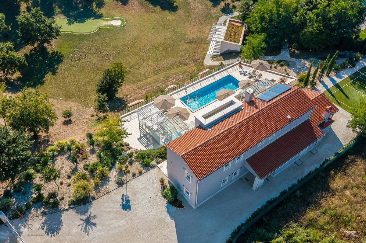Luftaufnahme der Villa mit Pool, Golf-Putting-Green und weitläufiger Landschaft.