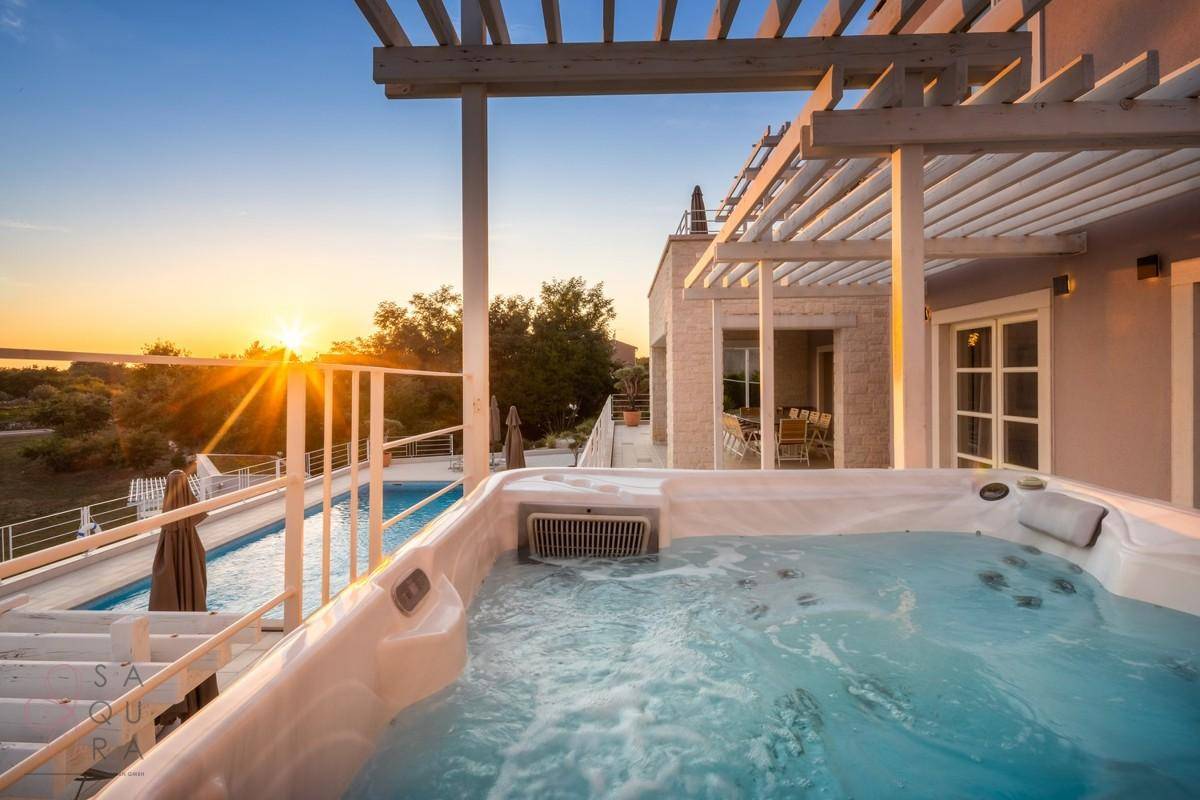 Luxuriöser Whirlpool auf der Terrasse mit atemberaubendem Sonnenuntergang und Poolblick.
