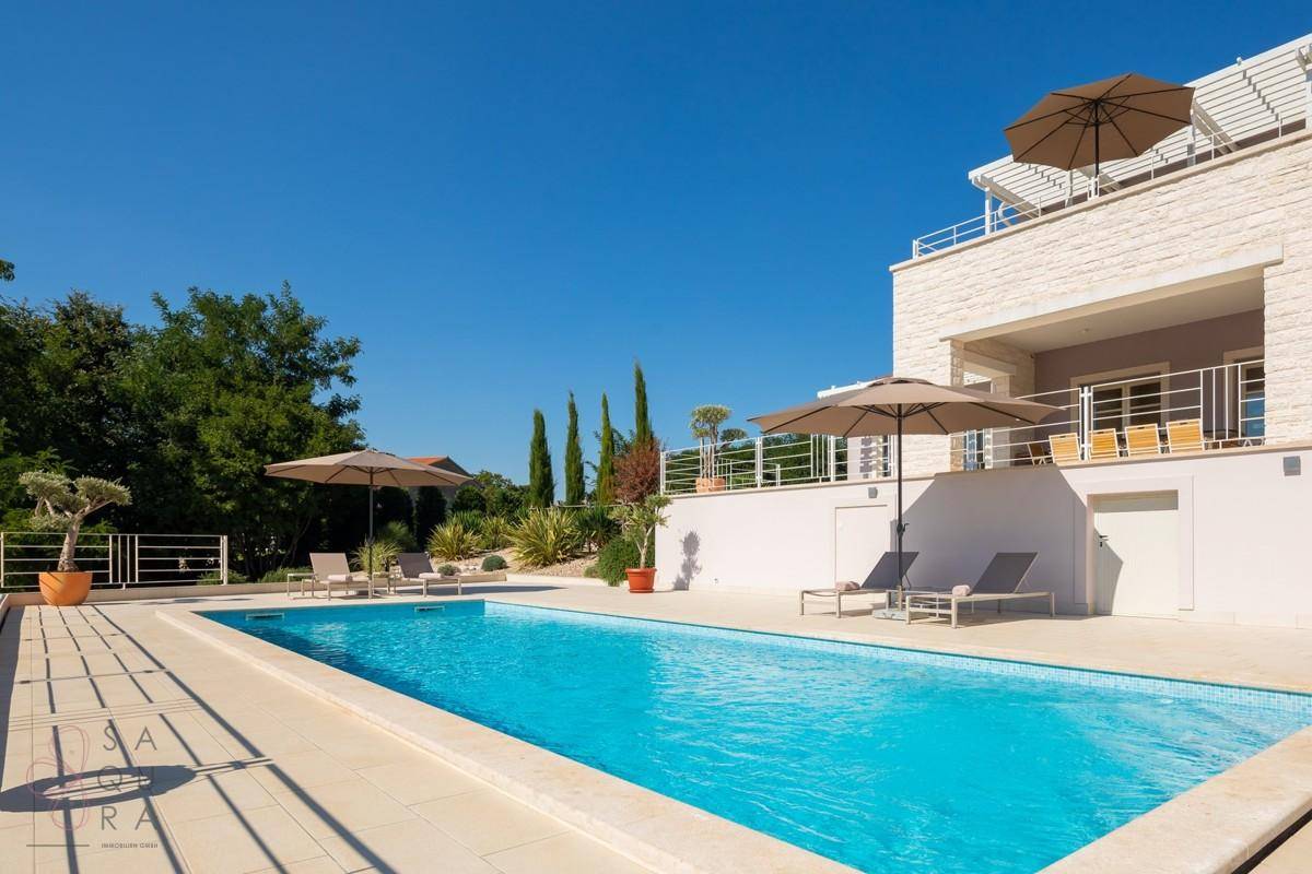 Entspannender Poolbereich mit Liegestühlen und Sonnenschirmen vor der modernen Villa.