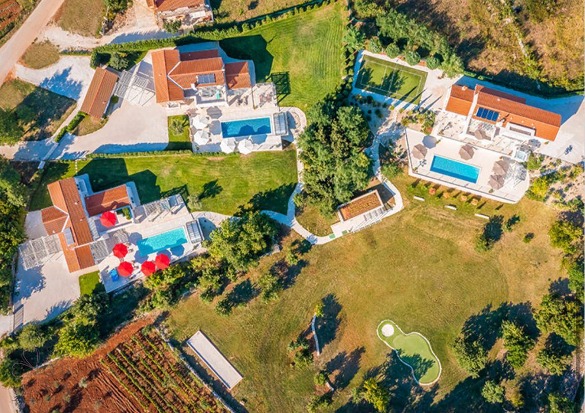 Luftaufnahme einer luxuriösen Wohnanlage mit mehreren Villen, Pools und weitläufigen Grünflächen.